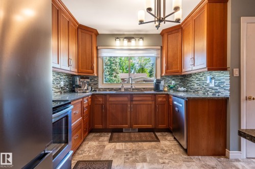 U-shaped kitchen featuring wood cabinetry, stainless steel appliances, and a mosaic tile backsplash - 14708 108 Av, Edmonton, AB 