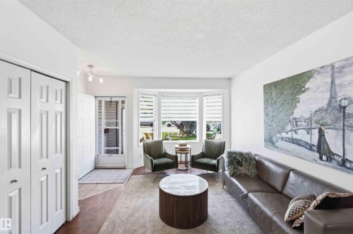 Living area featuring a prominent bay window with horizontal blinds, wood-finish flooring, white walls, and a track lighting fixture - 18808 72A Avenue, Edmonton, AB 