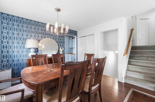 Dining area featuring wood-finish flooring, a contemporary chandelier, and a geometric pattern accent wall - 18808 72A Avenue, Edmonton, AB 