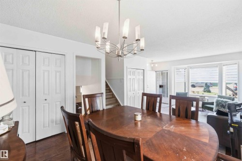 Open-concept dining area featuring a contemporary chandelier, rich wood-finish flooring, and white bi-fold closet doors - 18808 72A Avenue, Edmonton, AB 