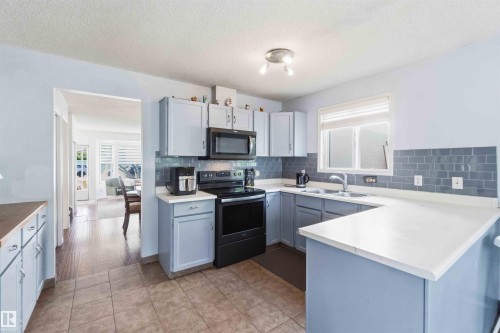 Kitchen featuring L-shaped white countertops, light blue cabinetry, a stainless steel sink, and a black range and microwave - 18808 72A Avenue, Edmonton, AB 