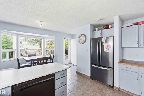 Kitchen featuring a bay window, light-toned cabinetry, stainless steel refrigerator, white countertops, and tile flooring - 18808 72A Avenue, Edmonton, AB 