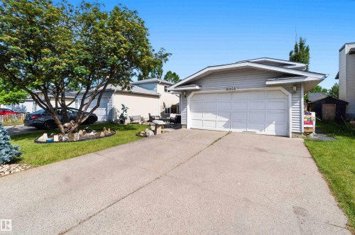 Front exterior featuring light gray siding, an attached two-car garage with a white door, a paved driveway, and a manicured lawn - 18808 72A Avenue, Edmonton, AB 
