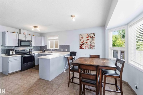 Spacious eat-in kitchen with tile flooring, light gray cabinetry, white countertops, gray subway tile backsplash, and black appliances - 18808 72A Avenue, Edmonton, AB 