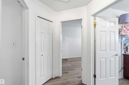 Hallway featuring wood-finish flooring, white paneled doors, and bright white wall finishes - 18808 72A Avenue, Edmonton, AB 
