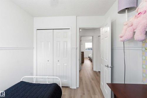 Interior room featuring bright white walls with wainscoting, wood-finish flooring, a white bi-fold closet, and a white interior door with brushed nickel hardware - 18808 72A Avenue, Edmonton, AB 