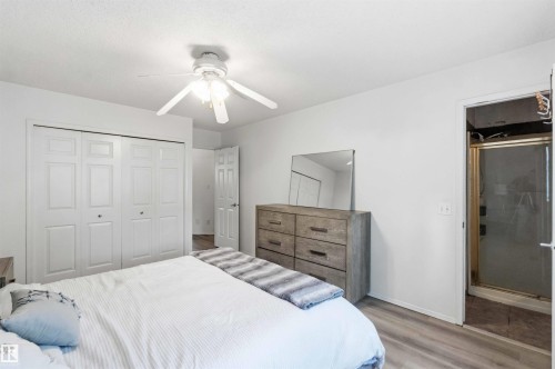 Bedroom featuring light-tone wood-finish flooring, a ceiling fan with integrated lighting, and white bi-fold closet doors - 18808 72A Avenue, Edmonton, AB 