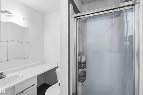Shower enclosure with sliding glass door, alongside a vanity featuring a single-basin sink, laminate countertop, and wall-mounted mirror - 18808 72A Avenue, Edmonton, AB 