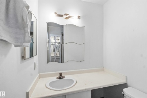 Bathroom vanity featuring an integrated sink with a single-handle faucet, a light-toned countertop, and a decorative wall mirror - 18808 72A Avenue, Edmonton, AB 
