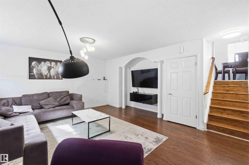 Open-concept living area featuring rich wood-finish flooring, a contemporary black pendant light, and recessed wall space for media - 18808 72A Avenue, Edmonton, AB 