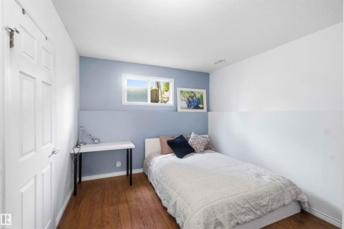 Room featuring wood-finish flooring, a two-tone painted wall, a white-framed window, and a white four-panel door - 18808 72A Avenue, Edmonton, AB 