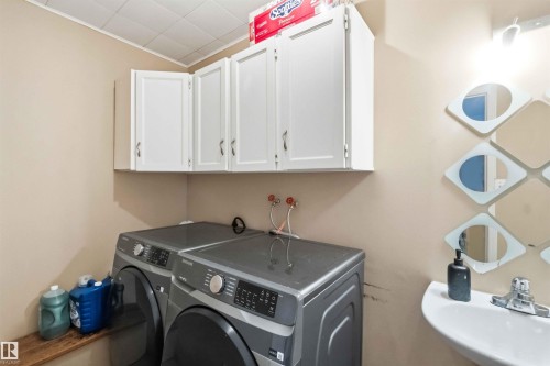 Laundry area featuring white upper cabinetry, a wall-mounted sink, and a decorative mirror installation - 18808 72A Avenue, Edmonton, AB 