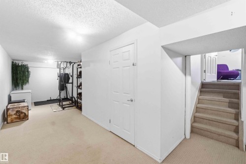 Carpeted lower level with recessed lighting, a white painted door, and staircase with carpeted treads - 18808 72A Avenue, Edmonton, AB 