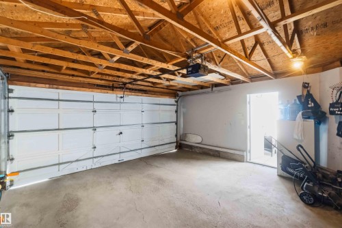 Spacious garage featuring an exposed wood beam ceiling, concrete flooring, a white paneled garage door, and a built-in electric garage door opener - 18808 72A Avenue, Edmonton, AB 