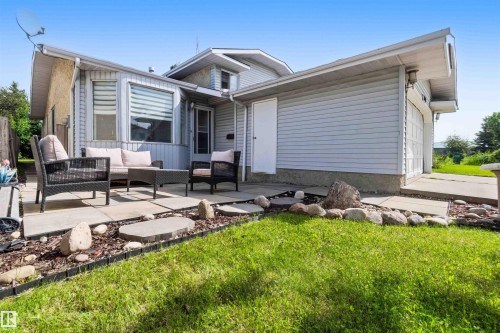 Rear exterior featuring an expansive concrete patio, a private side entrance, and an attached garage with a concrete driveway - 18808 72A Avenue, Edmonton, AB 