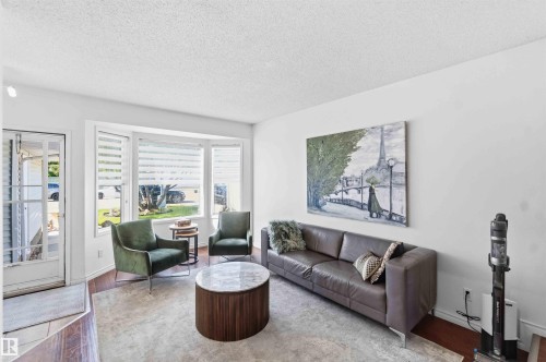 Living area featuring a bay window, wood-finish flooring, a white wall finish, and a glass-paneled entry door - 18808 72A Avenue, Edmonton, AB 