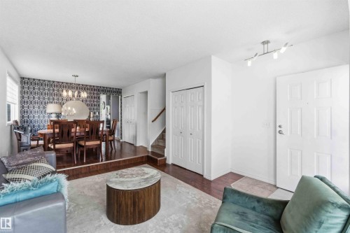 Sunlit living area featuring wood-finish flooring, a contemporary ceiling light fixture, and a white paneled entry door - 18808 72A Avenue, Edmonton, AB 