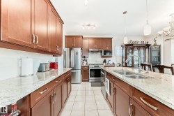 Kitchen featuring abundant wood cabinetry, light-toned countertops, stainless steel appliances, a center island with double sink, and tile flooring - 