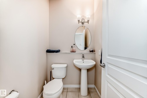 Pedestal sink with a wall-mounted oval mirror, illuminated by a brushed nickel vanity light fixture - 8730 180A Avenue, Edmonton, AB 