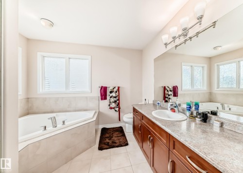 Bathroom featuring a corner soaking tub, dual windows, large vanity with double sinks, and extensive counter space - 8730 180A Avenue, Edmonton, AB 