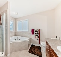 Bathroom featuring a corner soaking tub, a stand-up shower with a glass enclosure, dual windows, and a vanity with a countertop and built-in cabinetry - 