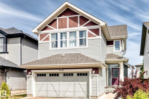 Two-story residence featuring light gray siding with maroon accent panels, a shingled roof, an attached two-car garage, multiple upper-level windows with white trim, and a prominent front entry with a purple door - 8730 180A Avenue, Edmonton, AB 