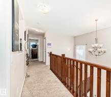 Upper-level landing featuring a wood-tone banister, recessed lighting, and a brushed nickel chandelier - 