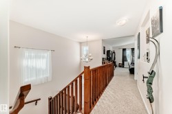 Carpeted hallway with a chandelier, wood banister, and natural light from a window - 