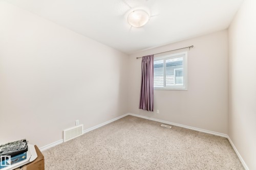 Carpeted interior room featuring a window with white trim, a flush-mount ceiling light fixture, and pale wall finishes - 8730 180A Avenue, Edmonton, AB 