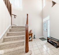 Bright entry foyer featuring a two-story ceiling, a white paneled door with decorative glass, and light-toned tile flooring - 