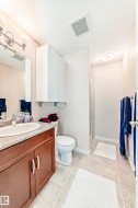 Bathroom featuring a wood-finish vanity with a light-toned countertop, a white toilet, and a stand-up shower enclosure - 