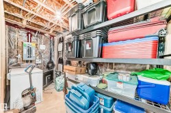 Unfinished basement area featuring exposed ceiling joists and wiring, a wall-mounted electrical panel, and built-in metal shelving - 