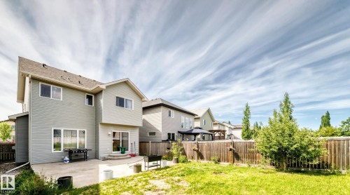 Expansive fenced backyard featuring a concrete patio, a sliding glass door, and green lawn - 8730 180A Avenue, Edmonton, AB 
