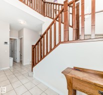 Foyer featuring a grand staircase with wood railings, a tiled floor, and a recessed ceiling light - 
