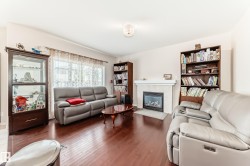 Spacious living area featuring rich wood-finish flooring, a contemporary fireplace with a tile surround and mantel, and large windows with sheer curtains - 