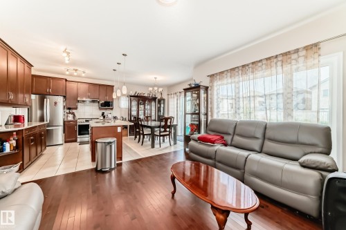 Open-concept main living area featuring wood-finish flooring, a kitchen with dark wood cabinetry and stainless steel appliances, a dining space with tiled flooring, and large windows with sheer coverings - 8730 180A Avenue, Edmonton, AB 