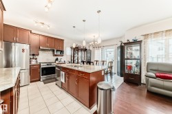 Kitchen featuring an island with a double sink, stainless steel appliances, wood-finish cabinetry, and light-toned tile flooring - 