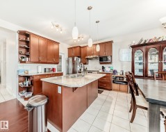 Kitchen featuring wood-finish cabinetry, light-toned countertop, stainless steel appliances, and a central island with a sink - 