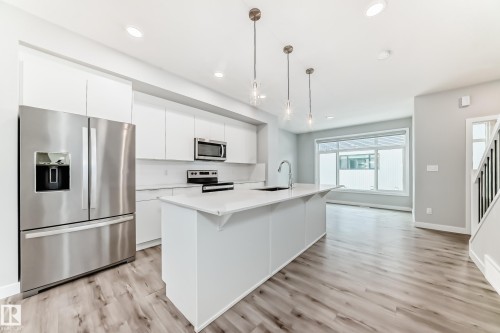 Modern kitchen featuring a large center island with integrated sink, stainless steel appliances, white cabinetry, and wood-finish flooring - 26 1729 Keene Crescent, Edmonton, AB 
