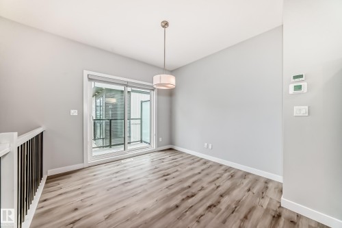 Room featuring wood-finish flooring, a contemporary ceiling light fixture, and a sliding glass door leading to an exterior balcony with black railings - 26 1729 Keene Crescent, Edmonton, AB 
