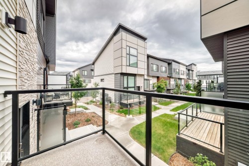 Modern exterior architecture with sleek lines, stone veneer accents, individual balconies with glass railings, landscaped grounds with concrete walkways, and manicured lawns - 26 1729 Keene Crescent, Edmonton, AB 