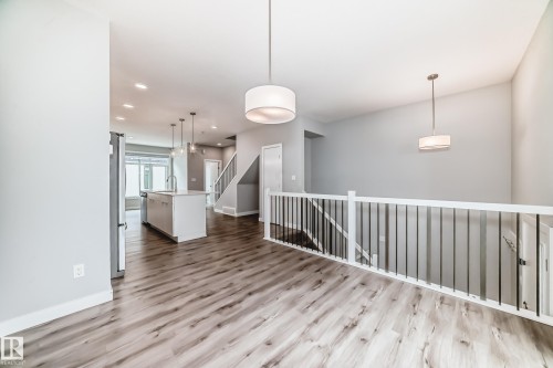Open-concept interior featuring wood-finish flooring, a contemporary kitchen island with a sink, stainless steel refrigerator, and modern pendant lighting - 26 1729 Keene Crescent, Edmonton, AB 