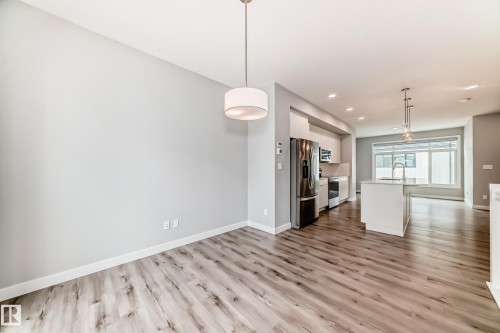 Spacious open-concept living area featuring wood-finish flooring, a contemporary drum pendant light fixture, and a neutral color palette - 26 1729 Keene Crescent, Edmonton, AB 