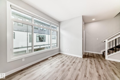 Spacious interior featuring wood-finish flooring, a contemporary staircase with white risers and black balusters, recessed lighting, and expansive windows - 26 1729 Keene Crescent, Edmonton, AB 