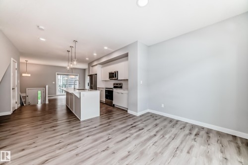 Open-concept living space featuring wood-finish flooring, a contemporary kitchen island with a sink and pendant lighting, stainless steel appliances, white cabinetry, and recessed lighting throughout - 26 1729 Keene Crescent, Edmonton, AB 