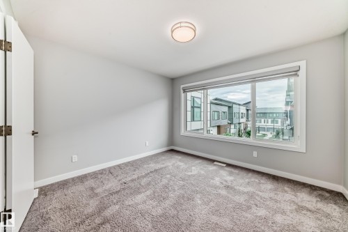 Carpeted room featuring a large window, neutral wall paint, white trim, and a ceiling-mounted light fixture - 26 1729 Keene Crescent, Edmonton, AB 