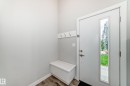 Entryway featuring a white door with a vertical window pane, built-in bench storage, white wall-mounted coat hooks, and wood-finish flooring - 26 1729 Keene Crescent, Edmonton, AB 