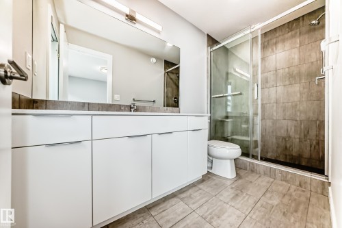 Modern bathroom featuring a white vanity with integrated pulls, a full-width mirror, and a frameless glass shower enclosure - 26 1729 Keene Crescent, Edmonton, AB 