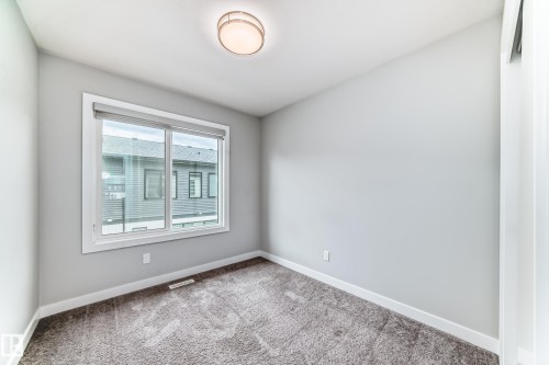 Room featuring light gray painted walls, a large window with white trim, gray carpet flooring, and a flush-mount ceiling light fixture - 26 1729 Keene Crescent, Edmonton, AB 