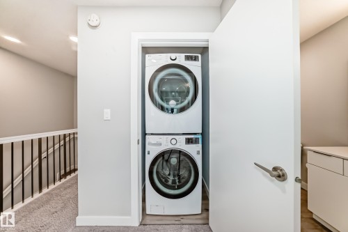 Dedicated laundry closet featuring a stackable washer and dryer, adjacent to a carpeted hallway with a white and black railing - 26 1729 Keene Crescent, Edmonton, AB 